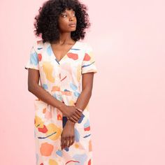 a woman standing in front of a pink wall wearing a dress with colorful shapes on it