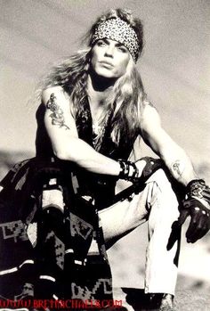 an old black and white photo of a man with long hair sitting on the ground