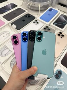 a person holding four different colored iphones in front of many other phones on display