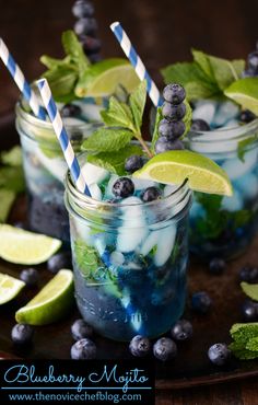 two glasses filled with blueberry mojitas and lime wedges on a table