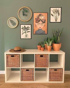 a white shelf with baskets and plants on it in front of a wall filled with pictures