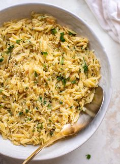 a bowl filled with pasta and parsley on top of a white tablecloth next to a silver spoon