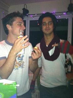 two men standing next to each other eating food