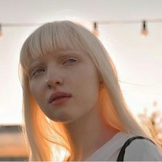 a woman with blonde hair and bangs standing in front of string lights, looking off to the side