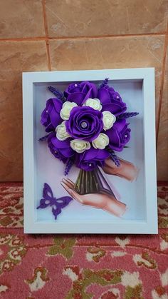 a bouquet of purple and white flowers in a frame on a carpeted floor next to a wall