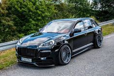 a black porsche cayen is parked on the side of the road with trees in the background