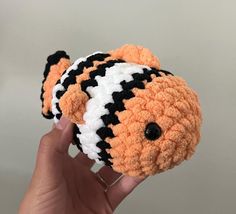 a hand holding a small orange and white teddy bear with black stripes on it's face