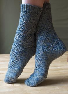 a woman's legs wearing blue socks with cabled design on them, standing on a wooden surface