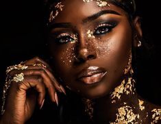 a woman with gold glitter on her face and hands, posing for a photo in front of a black background