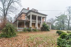 an old house in the fall with leaves on the ground and trees around it,