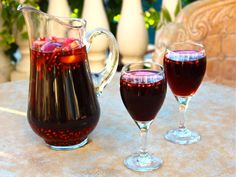 two glasses of red wine sit on a table with pitcher and cups next to it