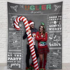 two people standing next to each other in front of a christmas photo booth with giant candy cane