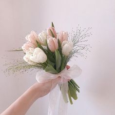 a hand holding a bouquet of white and pink tulips with greenery on it