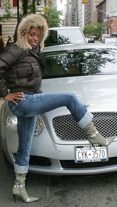 a woman sitting on the hood of a silver car in front of a city street