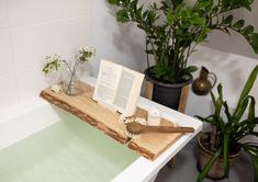 an open book on a wooden tray in a bathtub next to plants and flowers