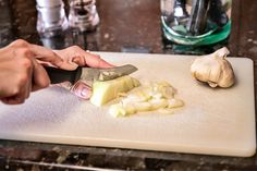 a person cutting up onions on top of a white cutting board with a large knife