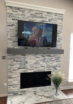 a flat screen tv mounted to the side of a fireplace in a living room next to a vase with flowers