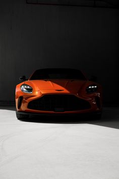 an orange sports car is parked in a dark room with its hood up and lights on