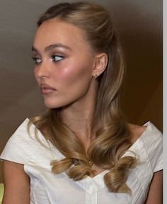 a woman with long blonde hair wearing a white shirt and earrings on her left ear