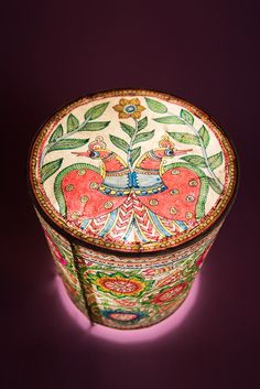 an ornately painted box with flowers and leaves on it's lid sits on a purple surface