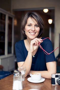 a woman sitting at a table with a cup of coffee and camera in front of her