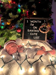 a baby laying on top of a white blanket next to a christmas tree with lights