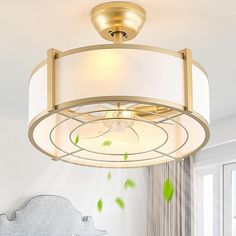 a light fixture in a bedroom with a white bed and green leaves on the ceiling