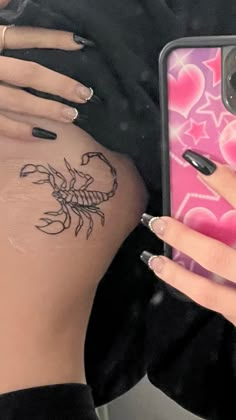 a woman's hand holding a cell phone with a scorpion tattoo on her stomach