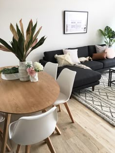 a living room filled with furniture and a wooden table surrounded by white chairs, potted plants