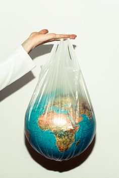 a person holding a plastic bag with the world in it's bottom half, on a white surface