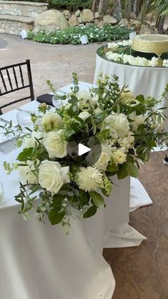 the table is set up with white flowers and greenery for an outdoor wedding reception