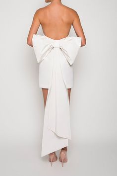 the back of a woman wearing a white dress with a large bow on it's shoulder