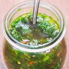 a glass jar filled with green liquid on top of a wooden table next to a spoon