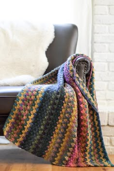 a multicolored crocheted blanket sitting on top of a leather chair next to a white brick wall