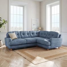 a blue sectional couch sitting on top of a wooden floor next to two large windows