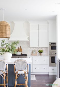 two wicker bar stools sit at the center of a kitchen island with white cabinets