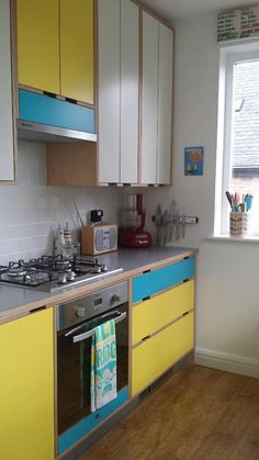 a kitchen with yellow and blue cupboards next to a stove top oven in front of a window