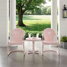 two pink chairs sitting next to each other on top of a porch near a tree