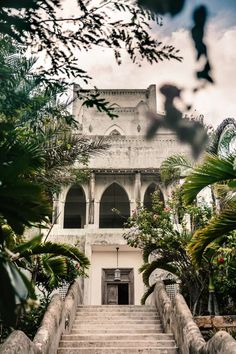 an old building with stairs leading up to the top and bottom floor, surrounded by greenery