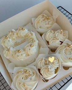 cupcakes with white frosting and gold decorations in a box on a cooling rack