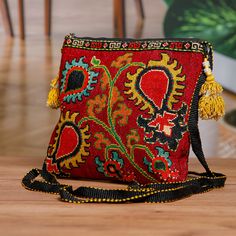 a red and black purse with tassels sitting on top of a wooden table