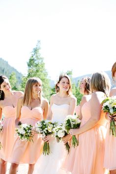 a group of women standing next to each other wearing dresses and holding bouquets in their hands