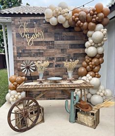 an outdoor table with balloons and decorations on the wall, including a wheelbarrow