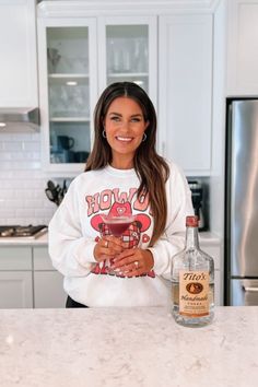 a woman standing in front of a counter with a bottle of booze next to her