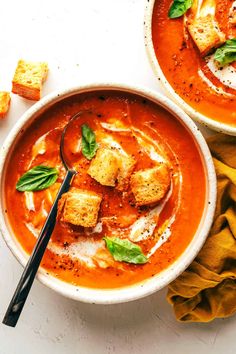 two bowls of tomato soup with tofu croutons and basil on the side