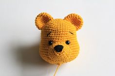 a crocheted yellow bear head on a white surface with a string attached to it