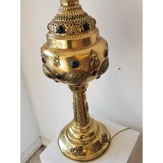 a gold colored lamp is sitting on a white pedestal with a black bead around the base