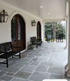 the front porch is lined with black chairs and white pillars, along with stone flooring