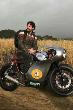 a man sitting on top of a motorcycle in the middle of a dirt road next to a field