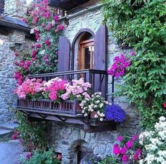 flowers are growing on the balcony of an old stone building with purple shutters and wooden balconies